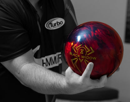 Person holding a red 'Black Widow' bowling ball with a blurred background